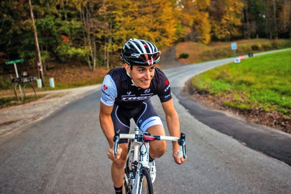 Man smiling while riding bicycle on road with fall foliage in background