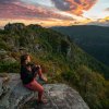 Woman sitting on rock looking out at mountain views and sunrise