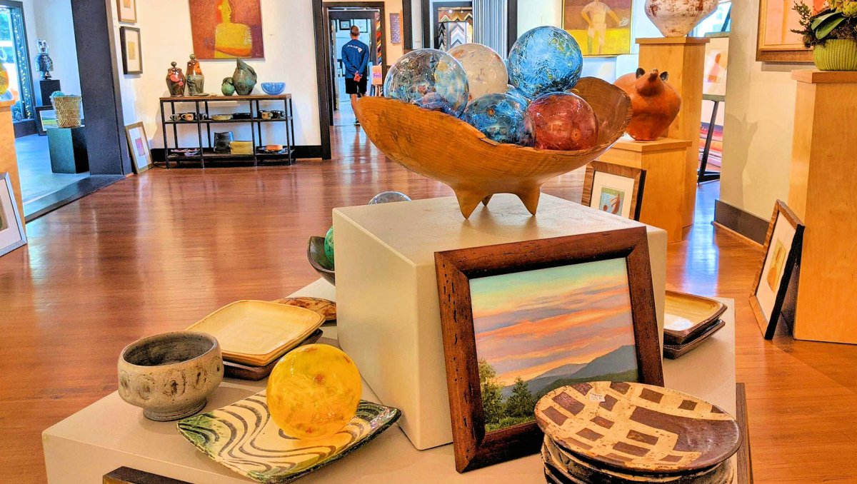 Display of art and pottery inside gallery with more art in background