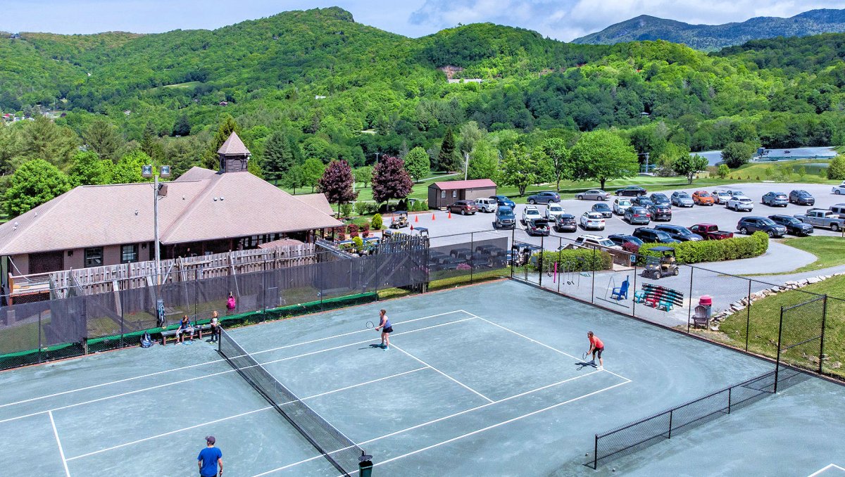 Aerial of people playing tennis on courts with clubhouse and mountains in background