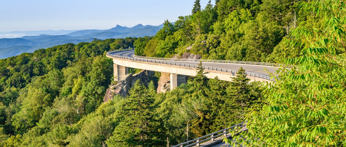 Linn Cove Viaduct surrounded by green trees and mountains in background on clear, bright day