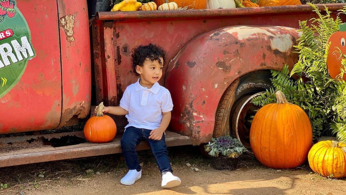 Toddler sitting on red truck holding a pumpkin
