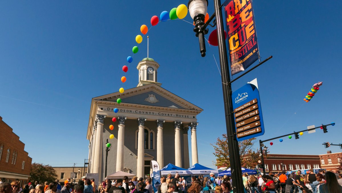 People enjoying festival in front of a courthouse with balloons and BBQ festival signage on light post