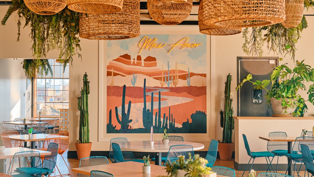 Interior of colorful restaurant with blue and orange chairs and tables in front of desert art on wall