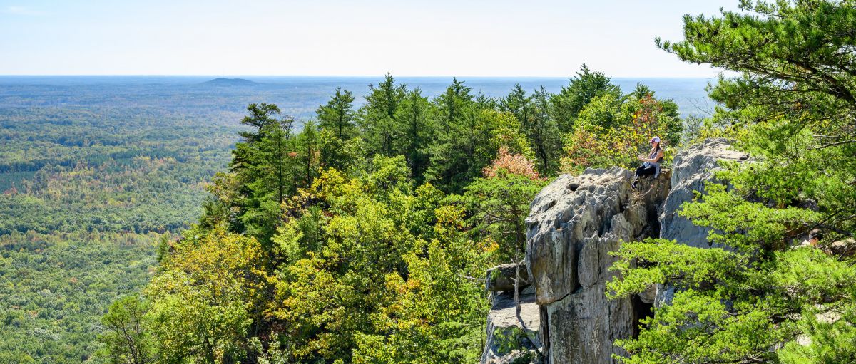 Woman sitting on edge of cliff at Crowders Mountain with trees all around on sunny day