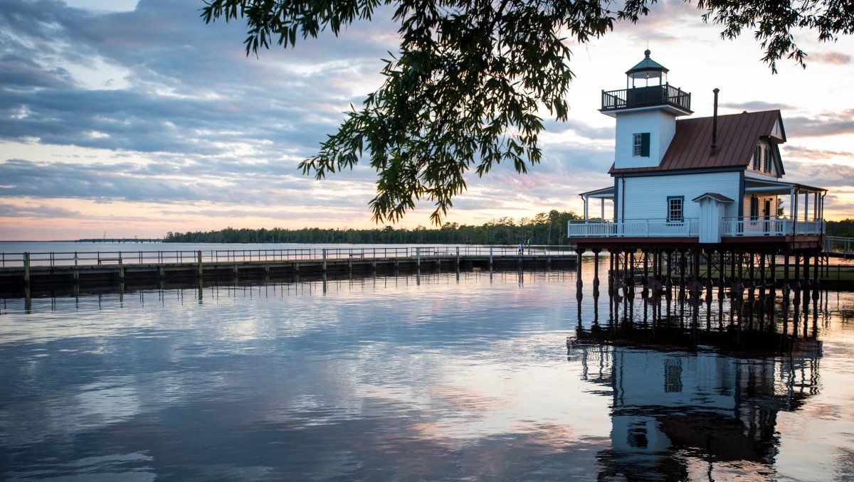 Horizontal shot of river lighthouse and cloudy sky reflecting into water during dusk