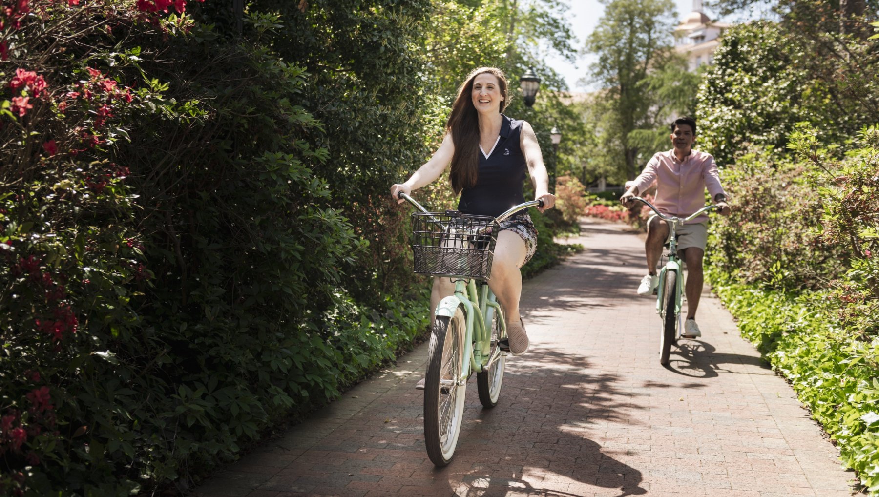 Couple riding bikes through brick path surrounded by trees and flowers