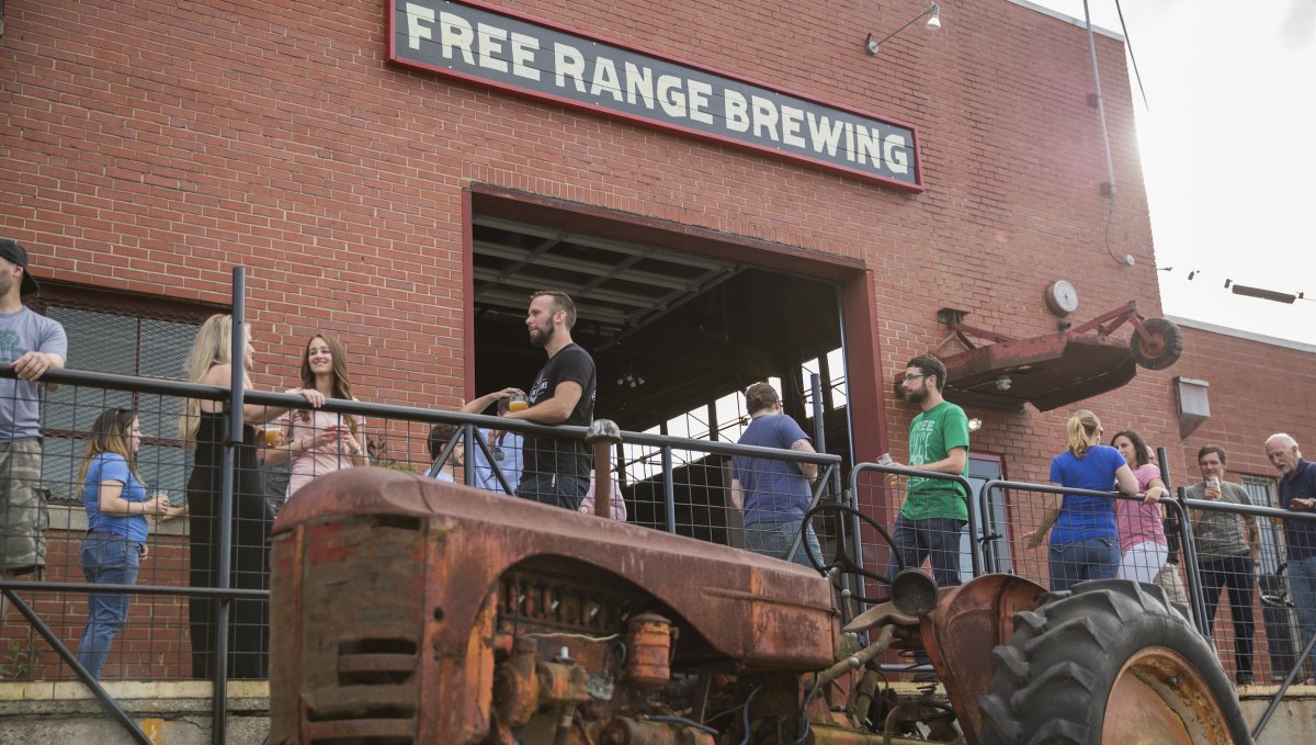 People standing outside Free Range Brewing enjoying beer and talking with a tractor in foreground