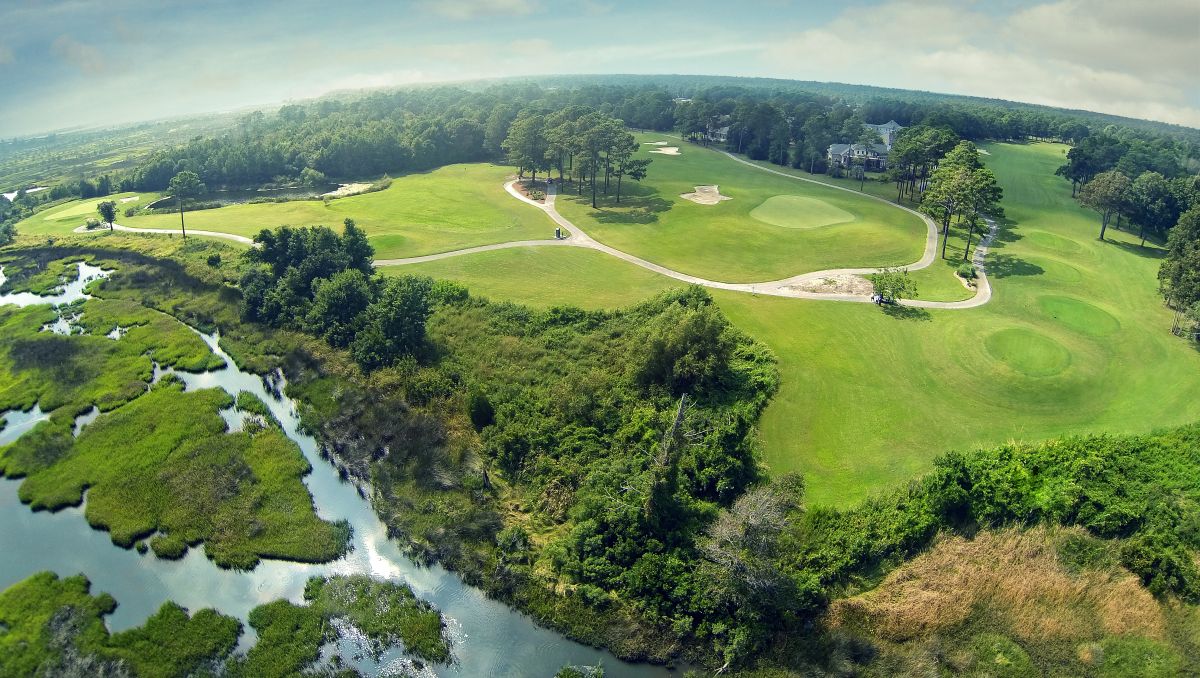 Aerial view of golf course greens, trees, marshes and cart paths on bright day