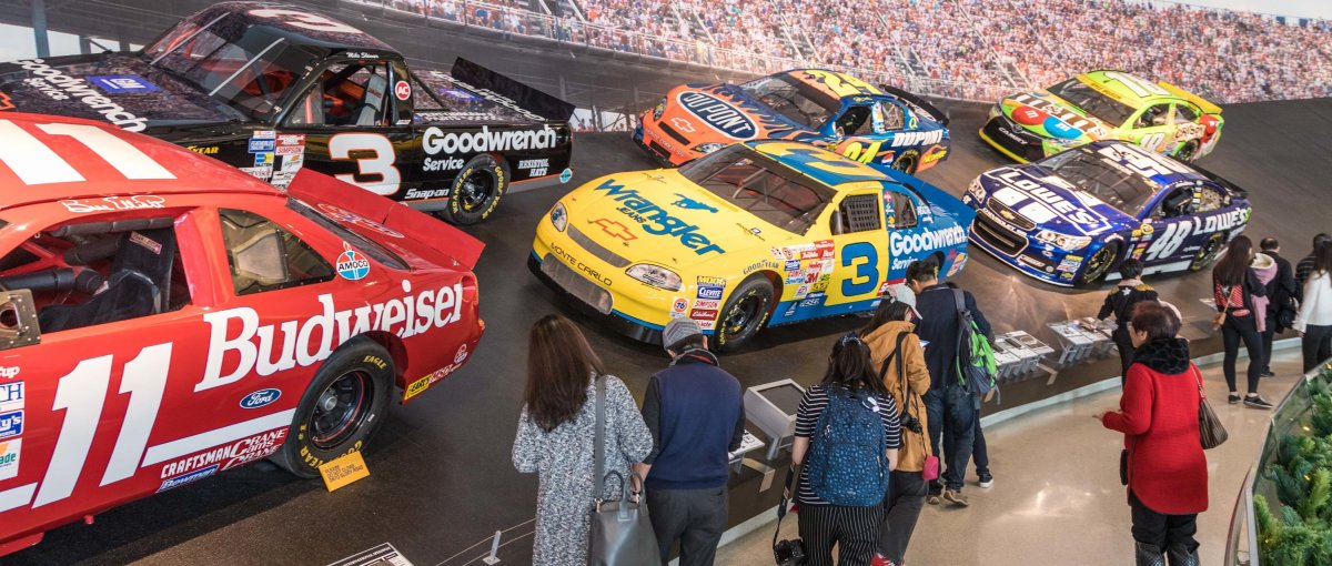 People looking at NASCAR Hall of Fame exhibit with cars on a banked speedway
