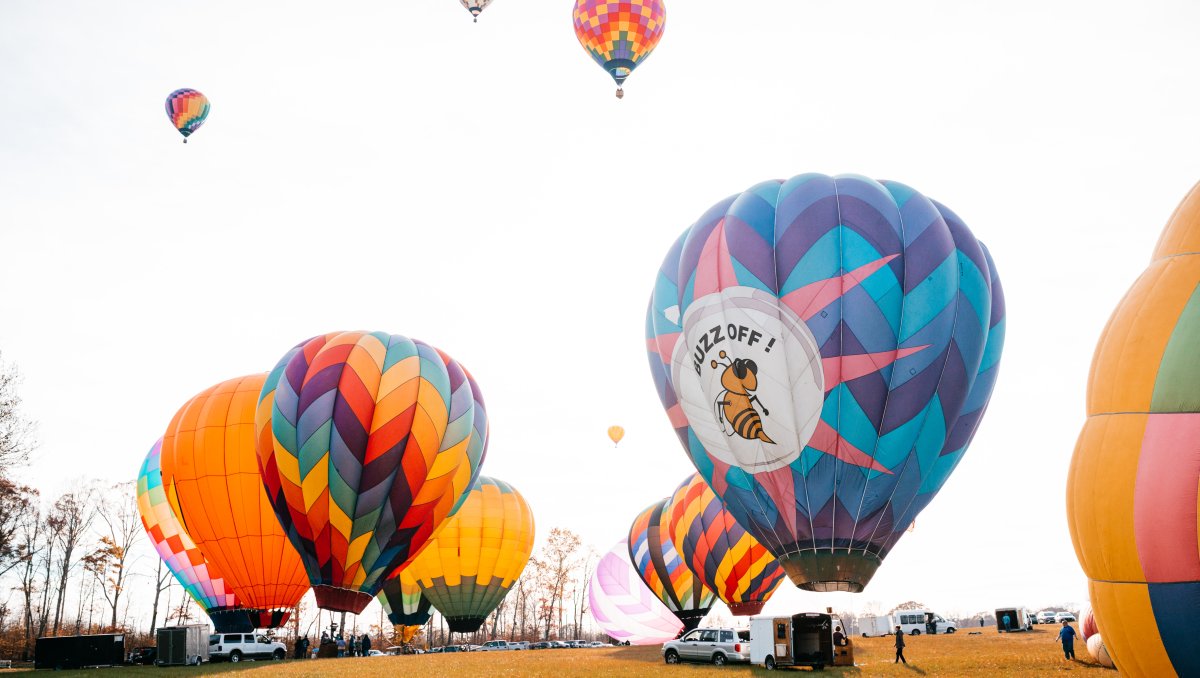 Many colorful hot air balloons waiting for takeoff on ground and some in air on gray day