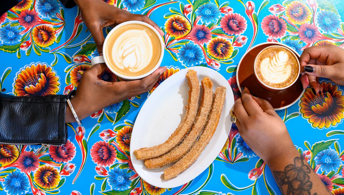 Hands holding cups of coffee with churros in the center of the table