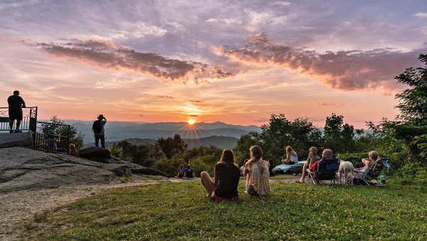 People sitting at lookout watching sunset over mountains in distance