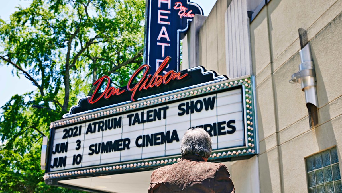 Person looking up at Don Gibson Theatre sign displaying acts
