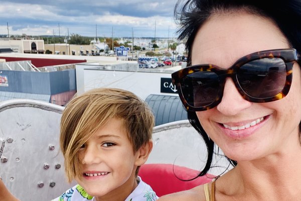 Woman smiling with son while riding Ferris wheel with boats in background during daytime