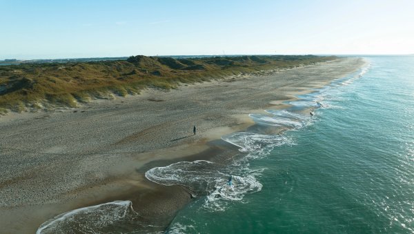 Aerial of beautiful, empty beach with waves rolling in and dunes in background