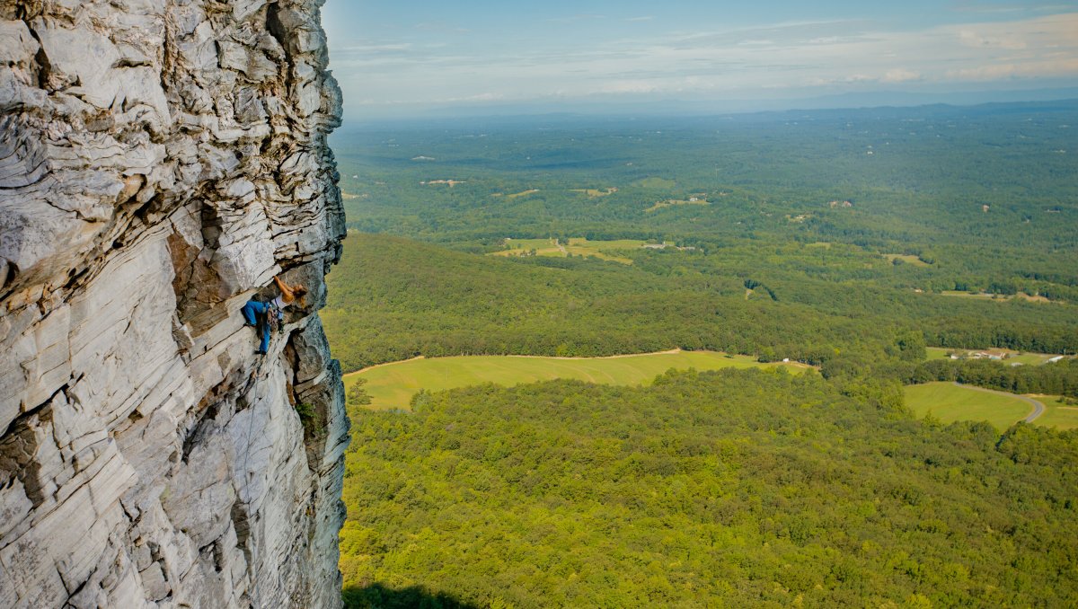 Person climbing cliffs at Hanging Rock State Park with valley below on sunny day