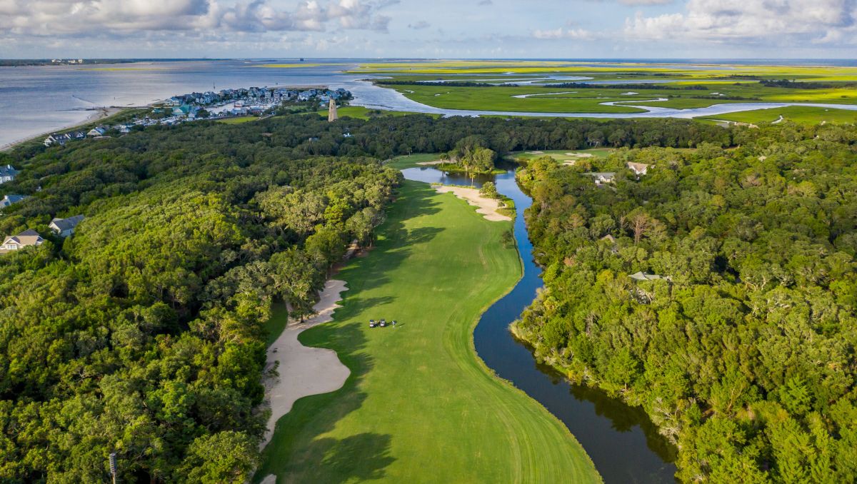 Aerial view of Bald Head Island Golf Club's golf course with trees, Old Baldy and waterways during daytime