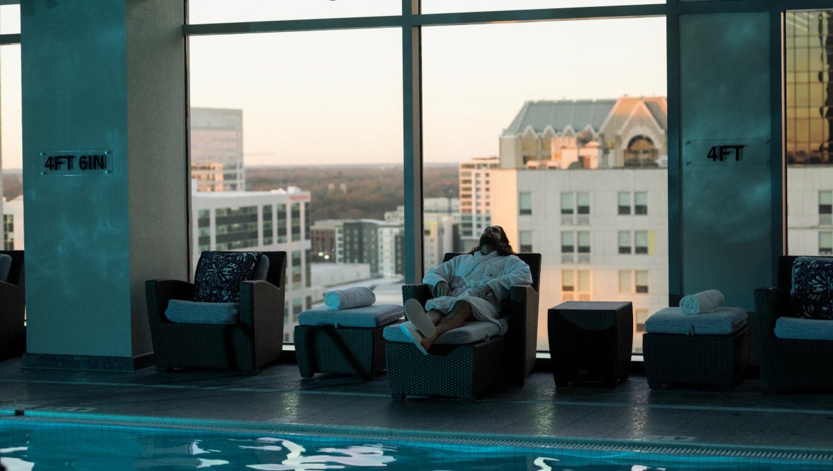 Man lounging by indoor pool at hotel with Charlotte buildings in background