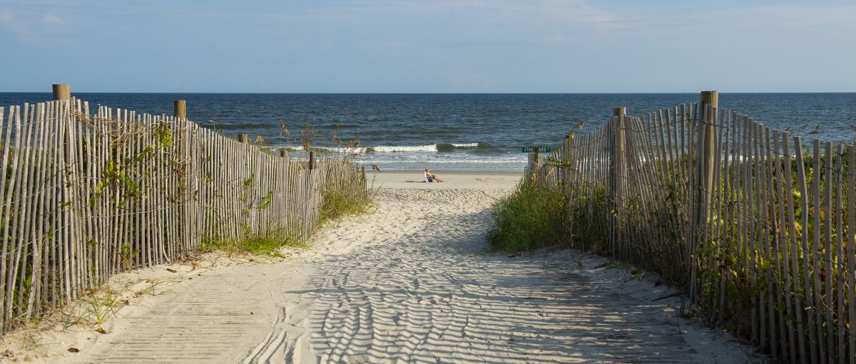 Beach access leading to man sitting on beach with ocean in background in N.C.'s Brunswick Islands