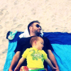 Man laying on beach towel in sand with nephew laying on top of him