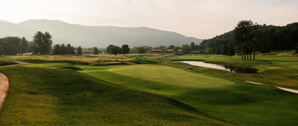 Empty golf course with clubhouse, trees and mountains in distance during daytime