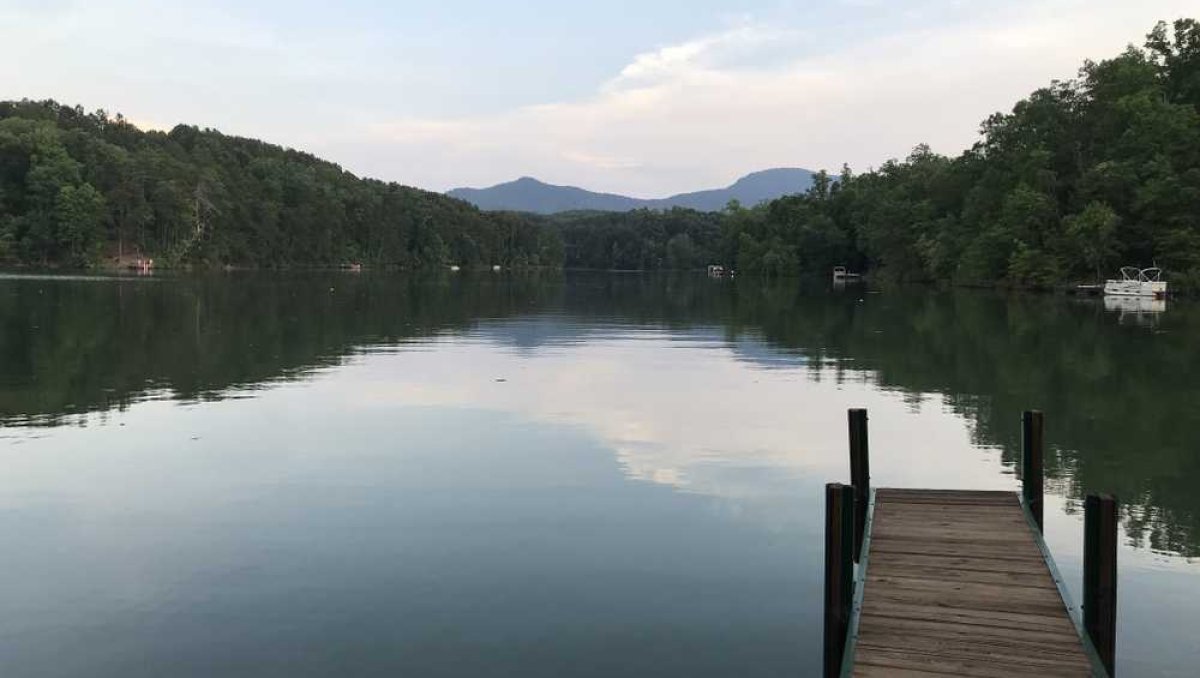 Dock extending into calm lake with tree-covered shoreline and mountains in distance