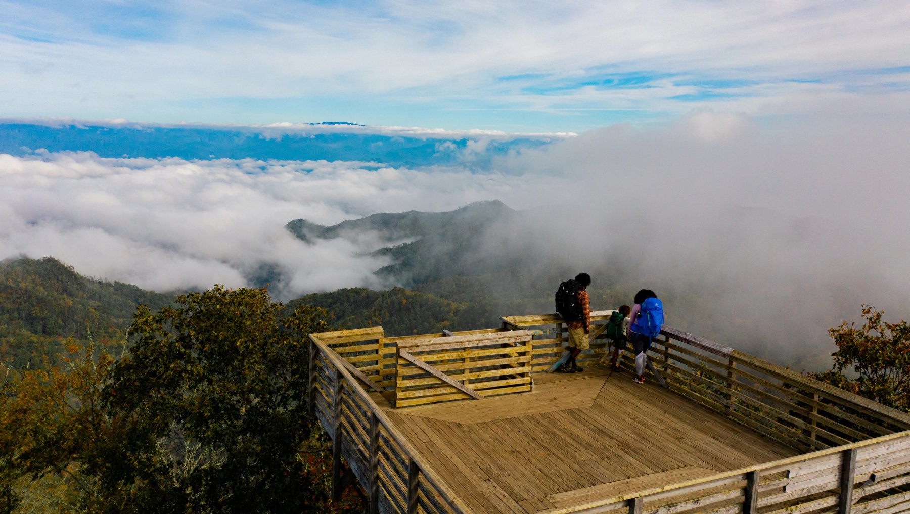 Family standing on top of wood tower overlooking mountains with low clouds