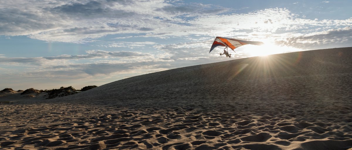 Hang glider in distance flying over sand dunes under sunny blue sky