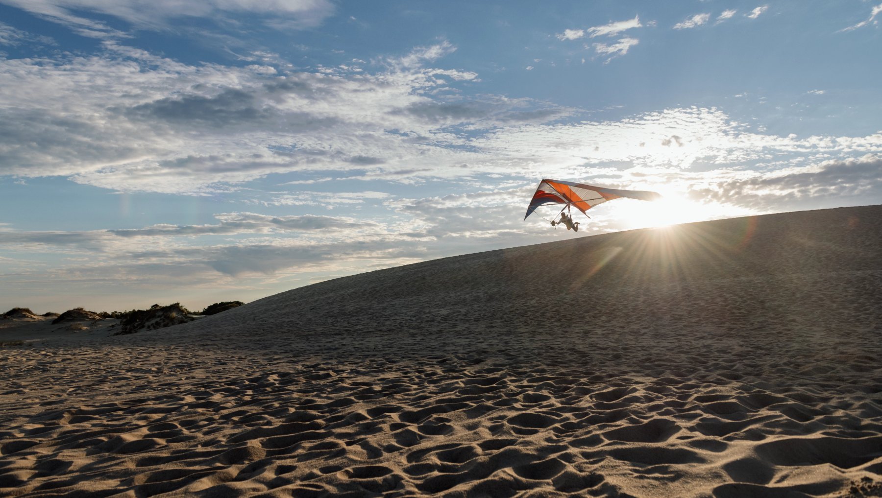 Hang glider in distance flying over sand dunes under sunny blue sky