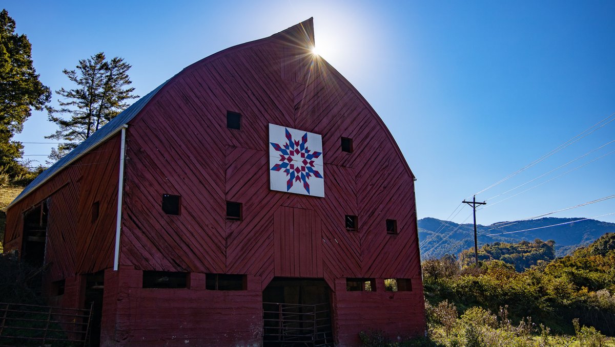 Sun shining on top of red barn with Quilt Block on its front