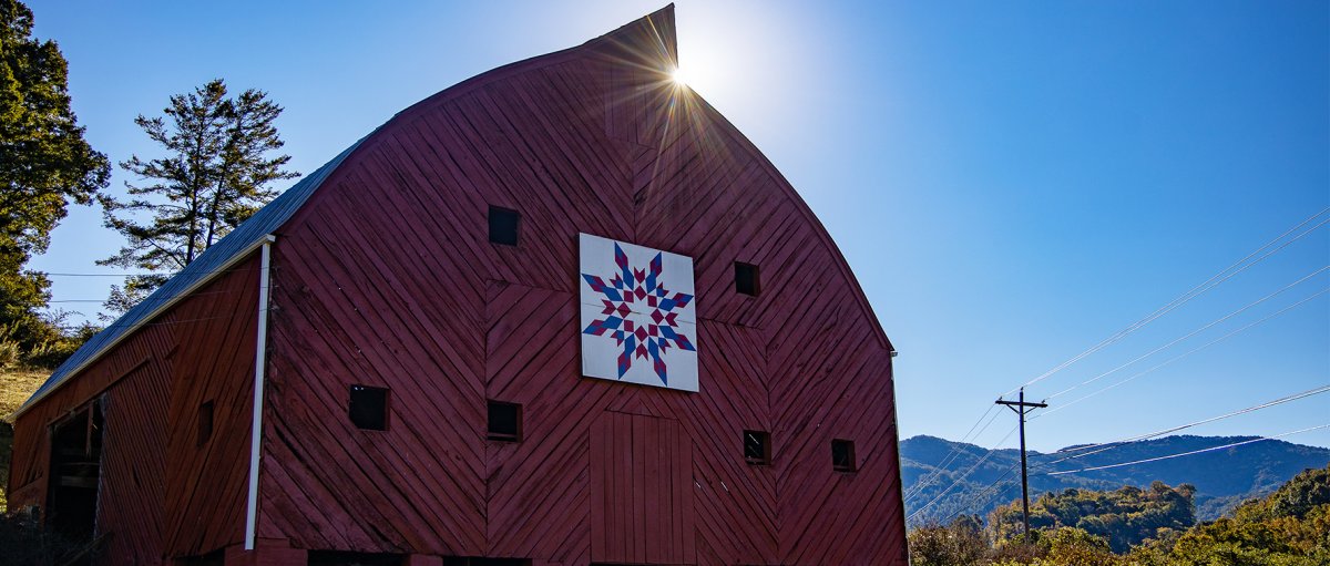 Sun shining on top of red barn with Quilt Block on its front