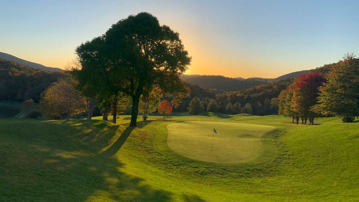 Serene golf course greens with sun setting over mountains in distance.