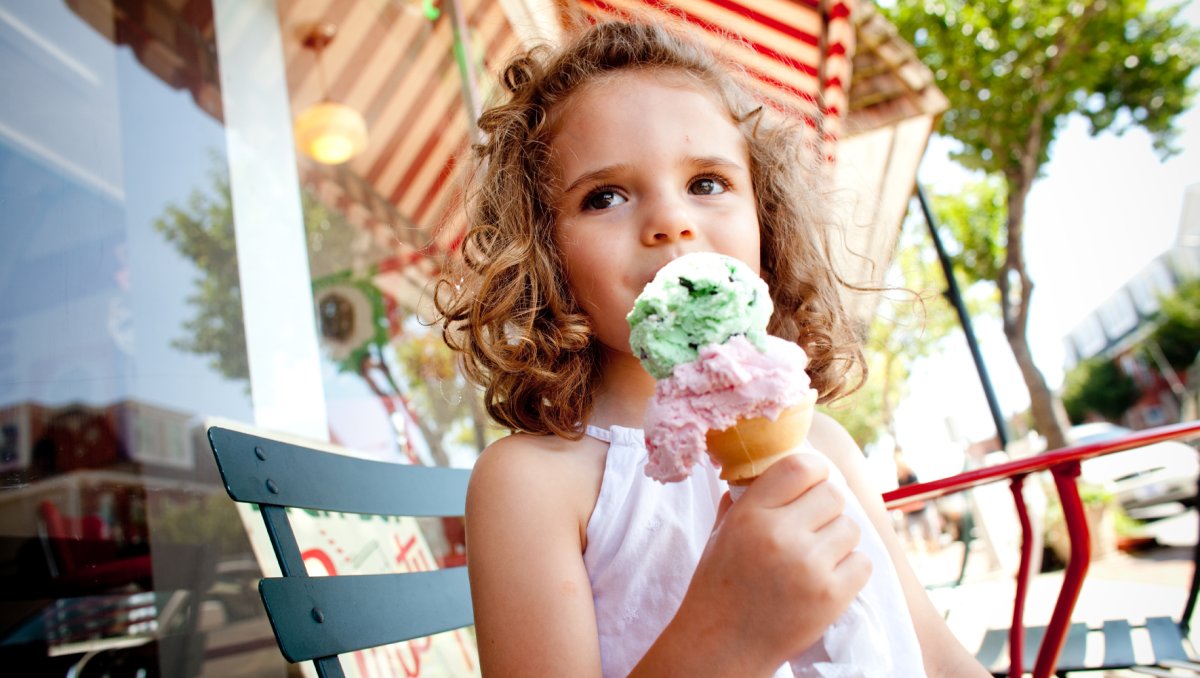 Little girl eating ice cream cone sitting on chair on sidewalk outside shop