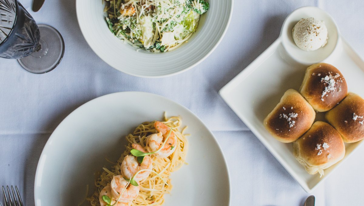 Overhead shot of entree, salad and bread on white tablecloth table