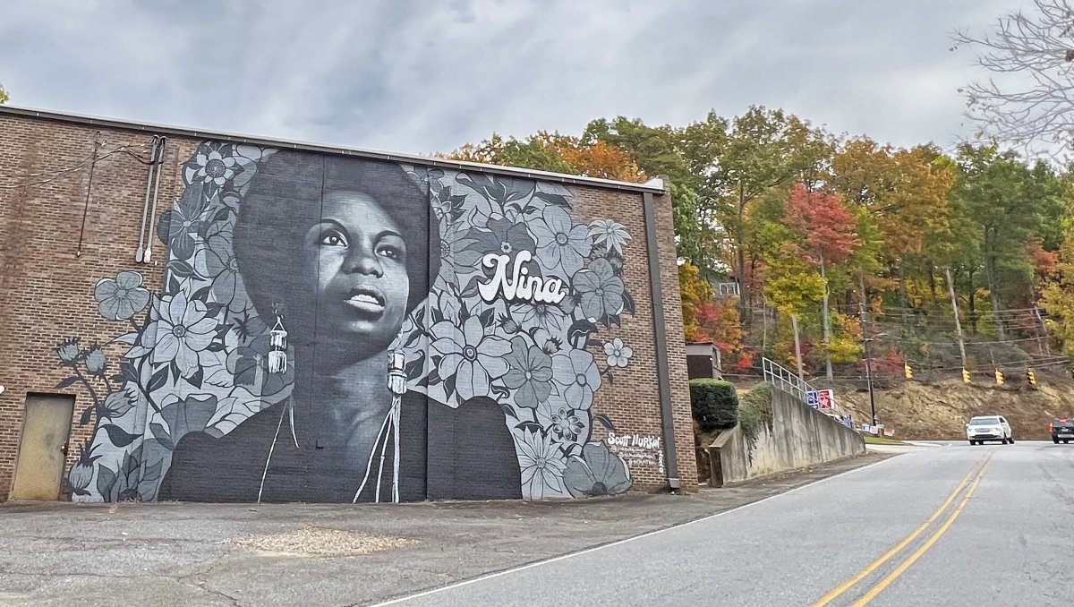 Nina Simone mural on the side of brick building beside road.