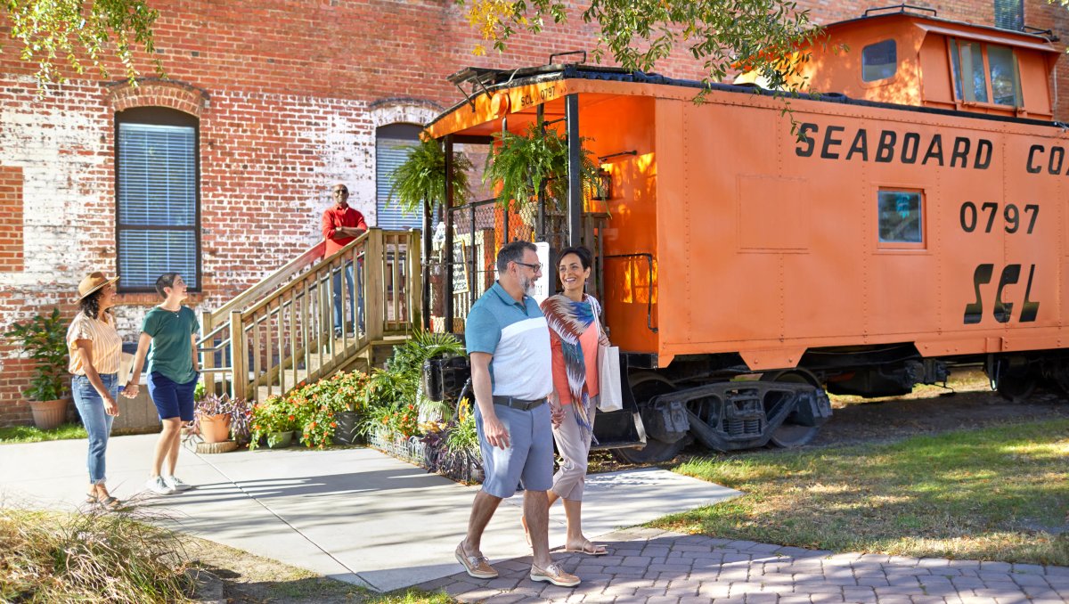 People exploring outdoor museum with train car exhibit in background