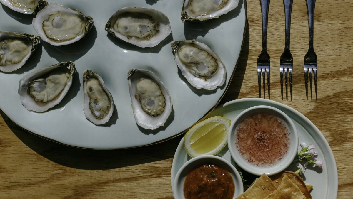 Plates of oysters and sauces sitting on wooden table at restaurant.