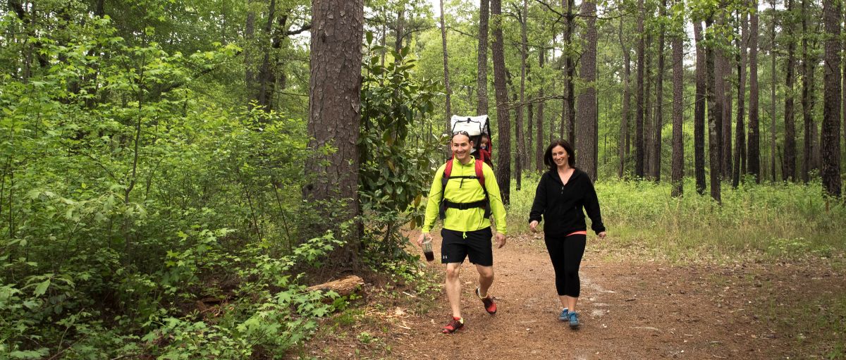 Man and woman walking on trail in Carvers Creek State Park with lots of green trees and foliage