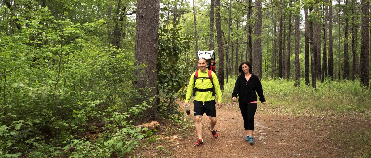 Man and woman walking on trail in Carvers Creek State Park with lots of green trees and foliage