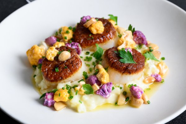 Plate of seared scallops and grits on table with glass of white wine