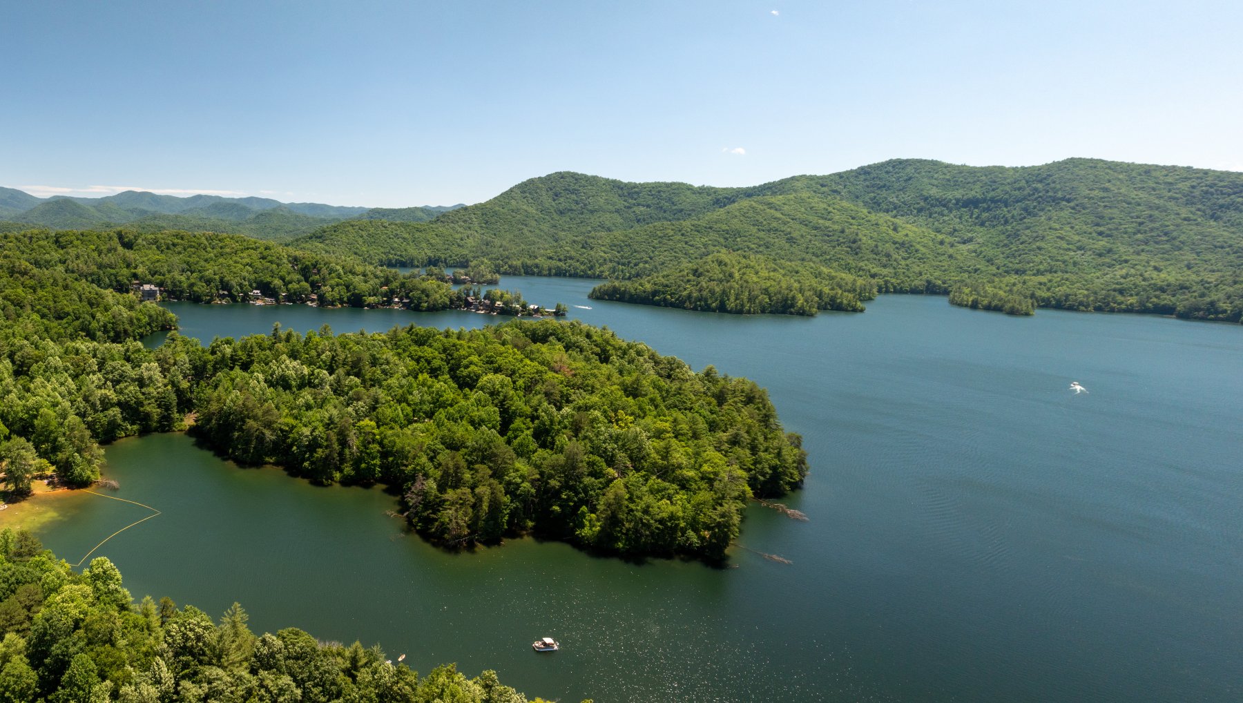 Aerial of Lake Santeetlah with boats in water surrounded by rolling hills and mountains in summer.