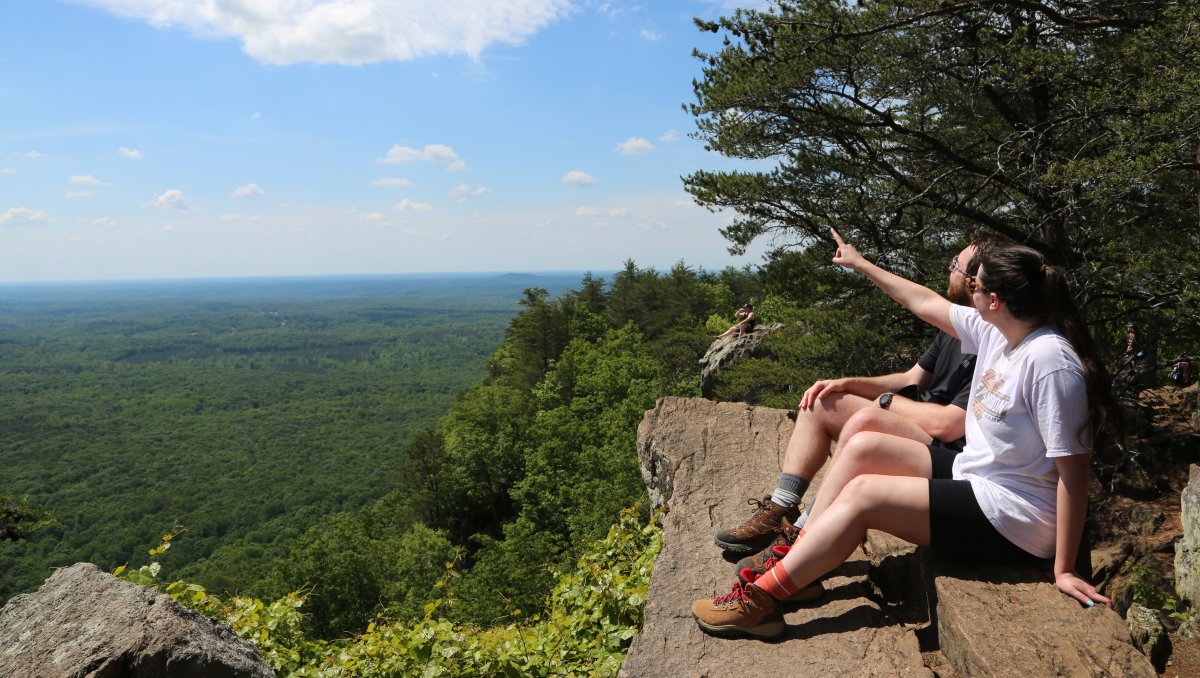 Couple sitting on rock outcropping at Crowders Mountain State Park with expansive view to the left.