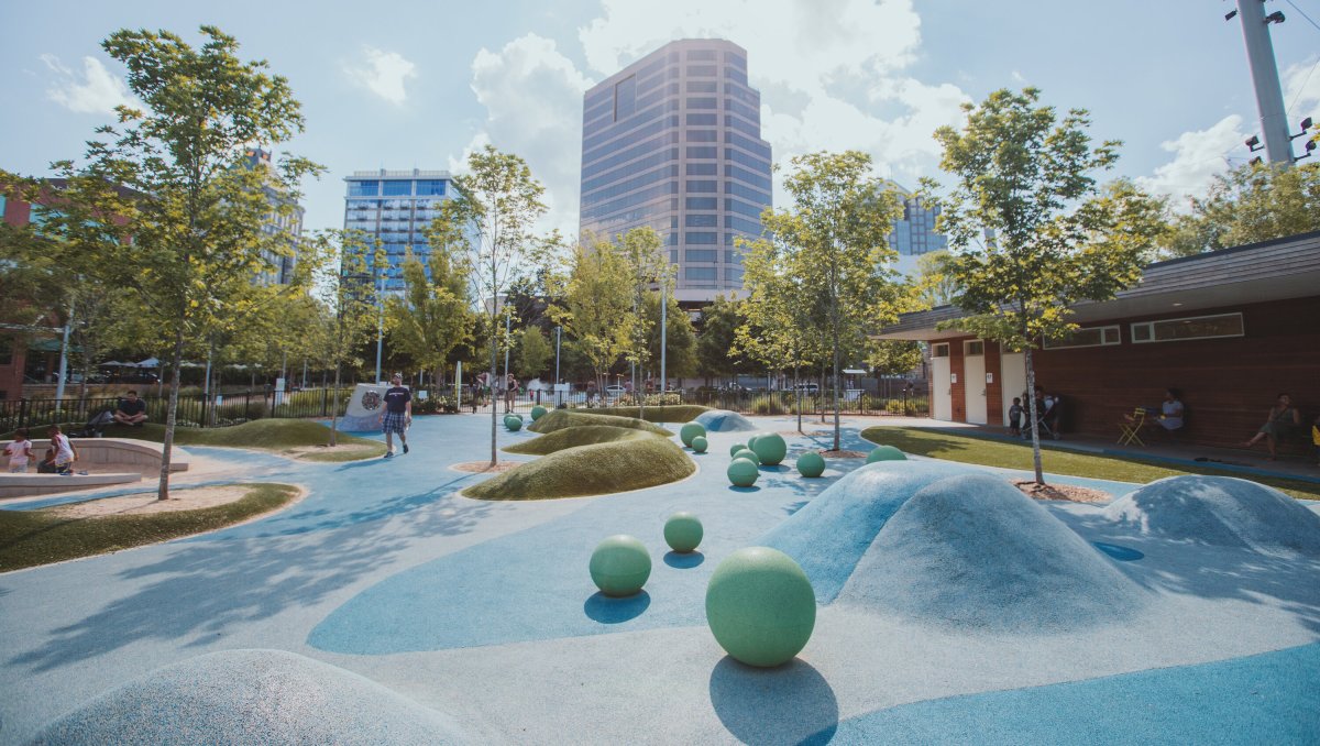 Park in between tall buildings in city with small trees and art in foreground