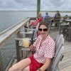 Woman holding up drink and smiling for camera sitting on a wood chair at waterfront bar