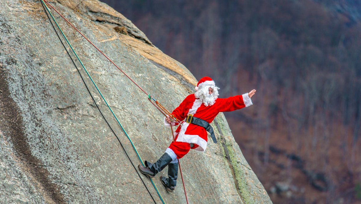 Person dressed as Santa repelling down Chimney Rock and waving to people below him