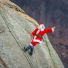 Person dressed as Santa repelling down Chimney Rock and waving to people below him