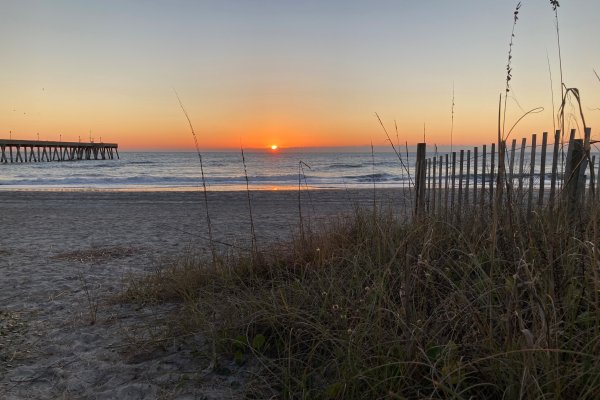 Sunrise over ocean on empty beach with pier jutting into water to the left