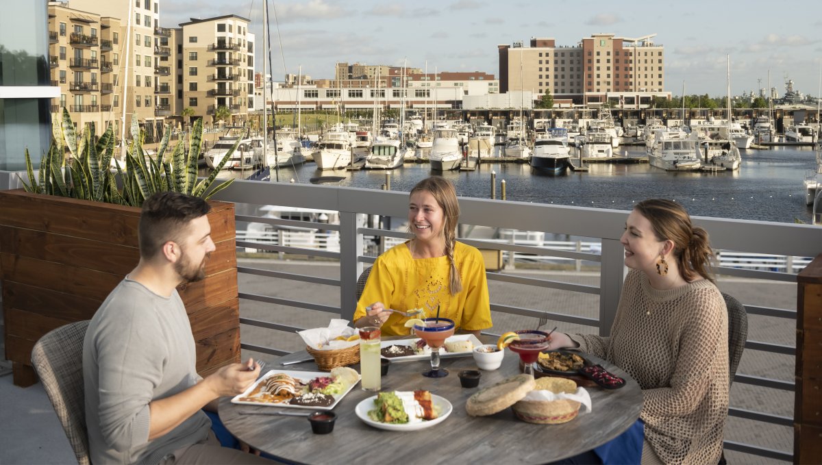 Friends enjoying drinks and a meal at waterfront restaurant in Wilmington with boats in background.