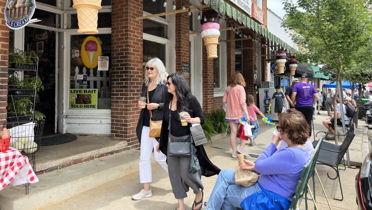 People walking on small-town street with local shops lining sidewalk.